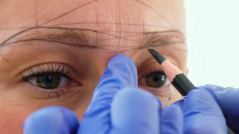 Beautician marking new eyebrow shape for microblading on female face closeup. Cosmetologist preparing for permanent tattooing