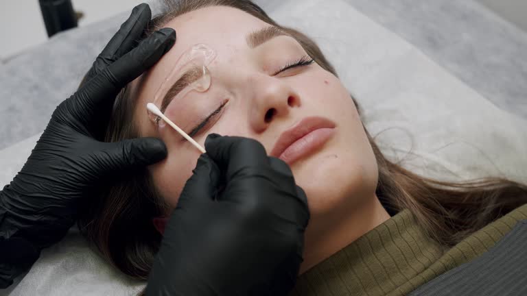 Master makes permanent eyebrow makeup procedure using special needle tattoo machine to woman in beauty salon. Microblading brows tattooing. Cosmetology procedure.