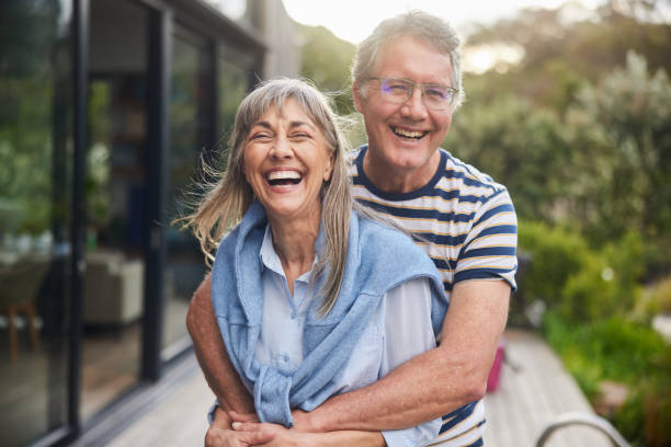 Mature couple standing arm in arm together and laughing outside in the back yard at home in summer